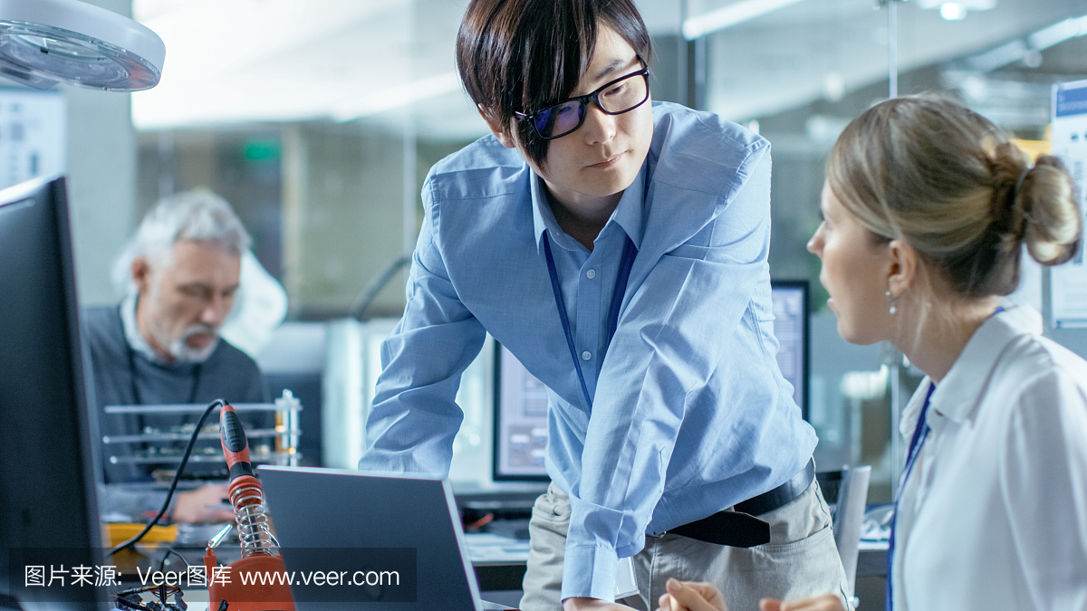 女計算機科學(xué)家用綠色屏幕模型連接電路板到她的筆記本電腦。她在先進技術(shù)實驗室工作。